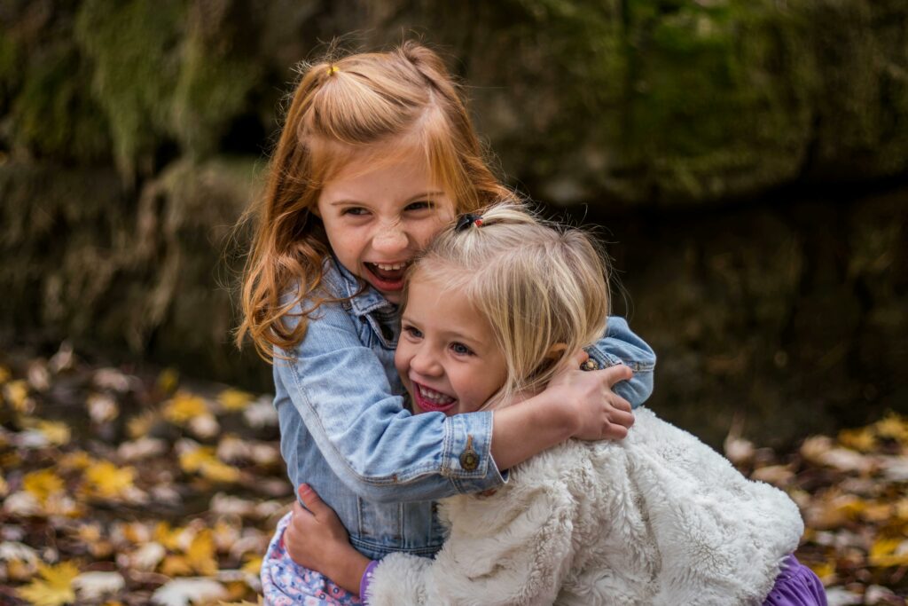 Two joyful sisters hugging outdoors in autumn, surrounded by fallen leaves.